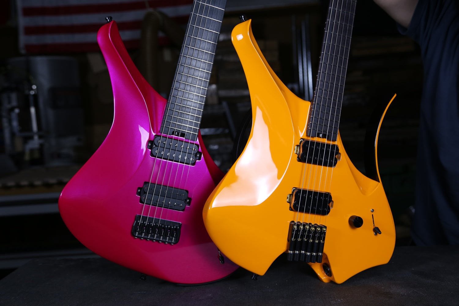 Two ergonomic electric guitars, one pink and one orange, on a dark surface.